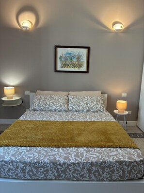 Ein Schlafzimmer mit einem Bett, zwei Nachttischlampen, einem gerahmten Kunstwerk an der Wand und einer gelben Tagesdecke.