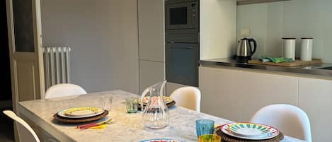 A modern kitchen with a marble countertop, white chairs, a large pendant light, and a microwave.