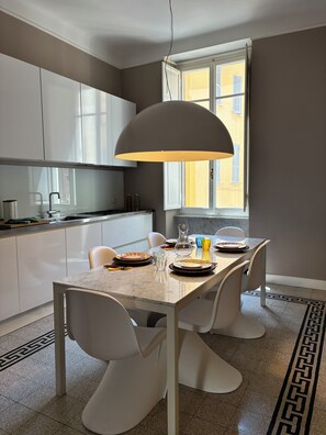 A modern kitchen with white cabinets, a marble countertop, and a dining area with a table set for four. - Rattazzi 36 - La Spezia & 5 Terre (ITALIA)