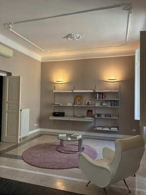Un salon moderne avec une table basse en verre, un fauteuil blanc, une bibliothèque et un radiateur.