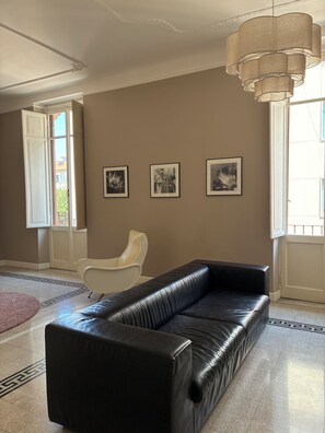 A living room with a black leather sofa, a white chair, and three framed pictures on the wall. - Rattazzi 36 - La Spezia & 5 Terre (ITALIA)