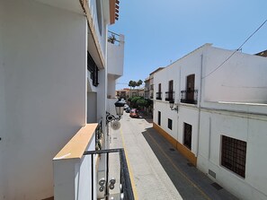 Eine enge Straße mit weißen Gebäuden, Balkonen und blauem Himmel.