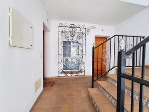 Eine Treppe mit schwarzer Geländer führt zu einer Holztür mit einem verzierten Metallgitter.