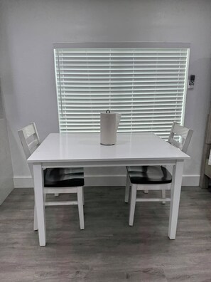 A white table with two chairs, a white vase, and a window with blinds. - Hale Haven - Luxury Stay in the Heart of Tampa! (Tampa)