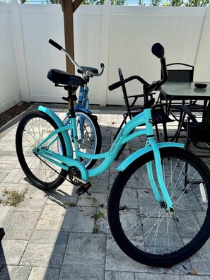Ein türkisblaues Fahrrad steht auf einer Terrasse mit einem weißen Zaun. Im Hintergrund befindet sich ein Tisch mit Stühlen.