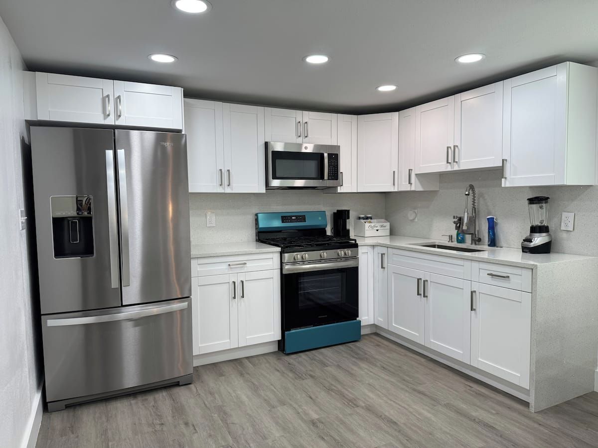 A modern kitchen with stainless steel appliances, white cabinetry, and a wood floor.
