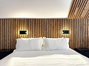 A modern bedroom with a wooden slat wall, a large bed with white bedding, and two wall-mounted light fixtures. - Upscale Loft (Thunder Bay)