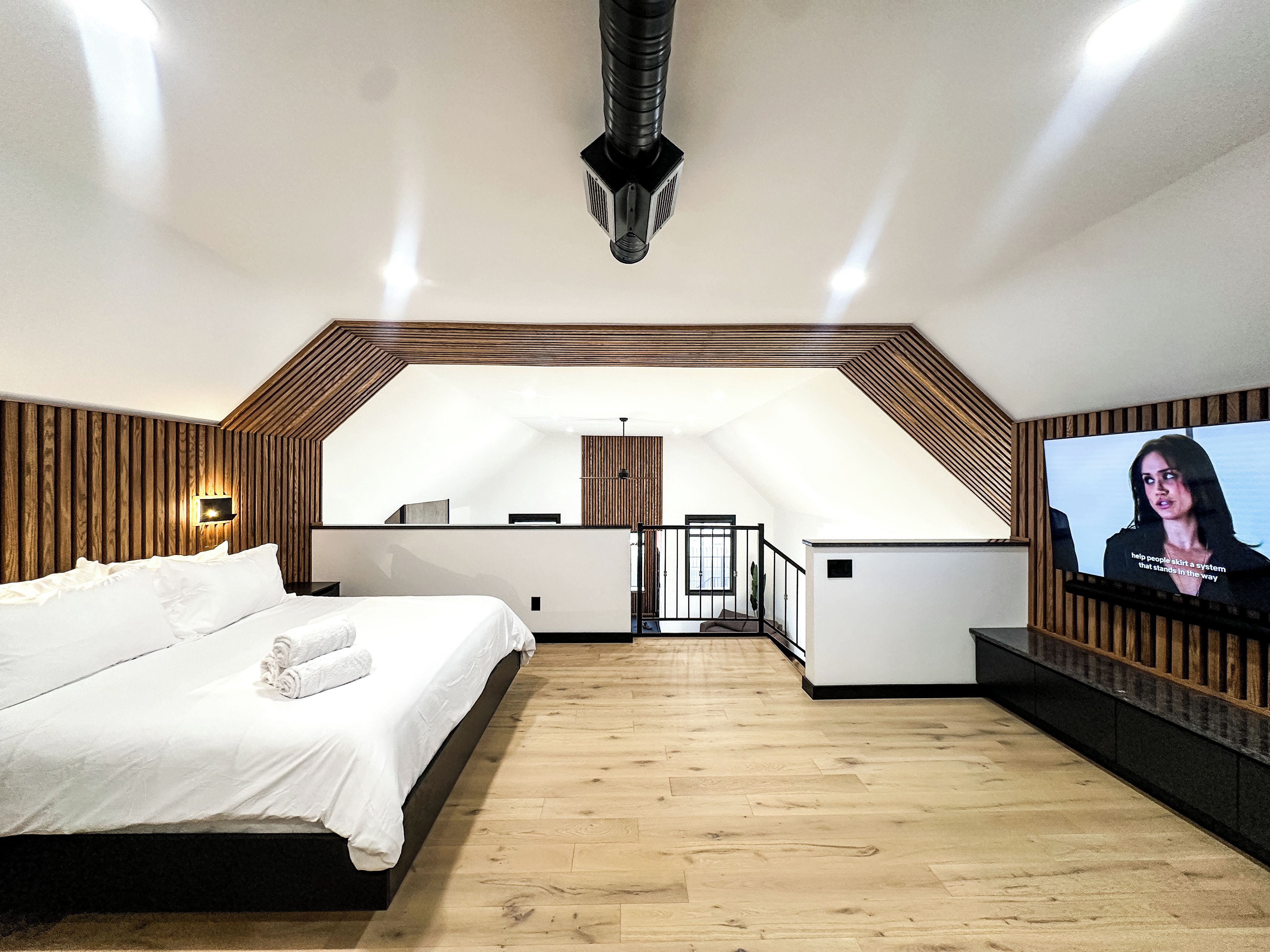 A bedroom with a large bed, a television, and a wooden ceiling.