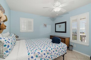 Ein Schlafzimmer mit einem Bett, einem Schminktisch, einem Deckenventilator und einem Fenster mit Fensterläden.