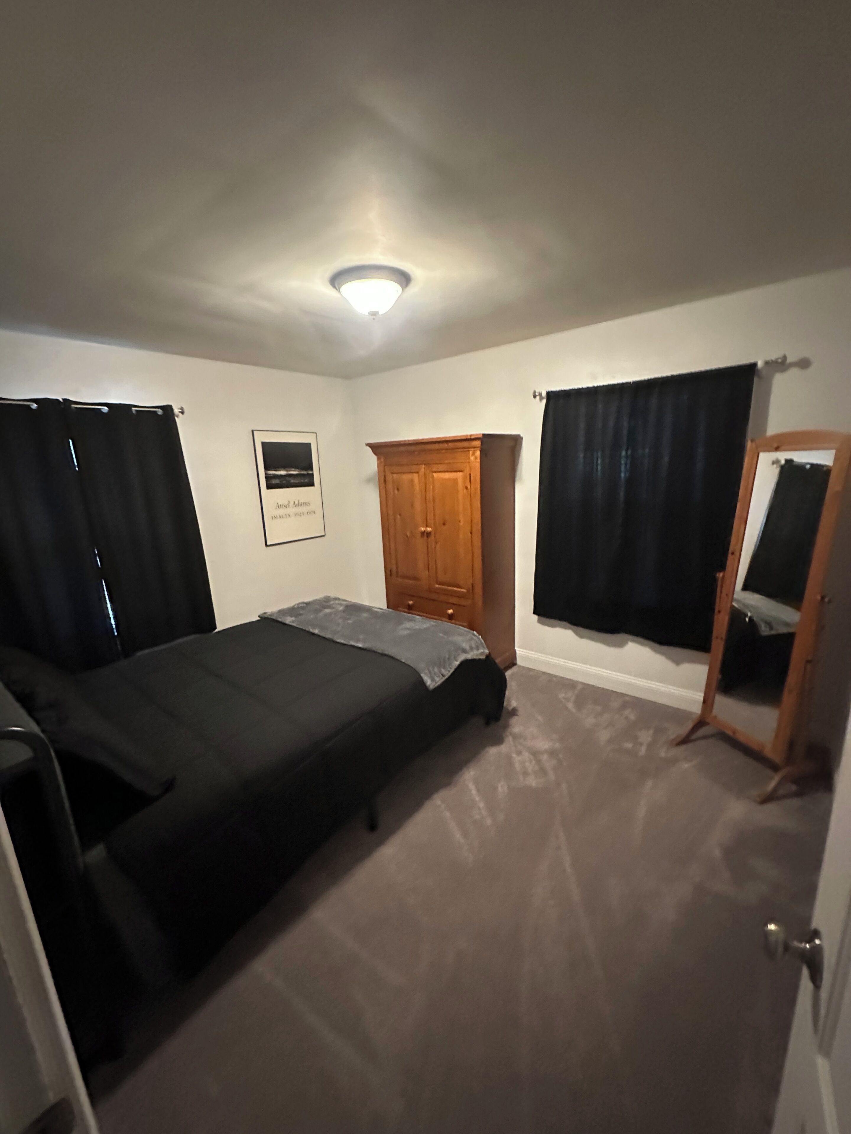 A bedroom with a bed, a wooden wardrobe, a mirror, and a framed picture on the wall.