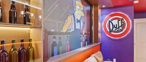 Un coin bar avec un canapé en cuir, un mur décoré d’un personnage de dessin animé et un panneau indiquant « Duff ».