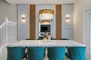 A dining room with a white table, teal chairs, a chandelier, and a TV in the background. - Marvelous 5 bedroom home for vacation in Orlando with private pool (Davenport)