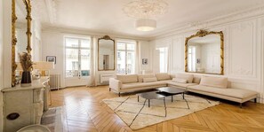 A spacious living room with a large sectional sofa, a coffee table, and a decorative rug. - Elegant 220m² Abode In Grands Boulevards: Expansive Living & Refined Interiors (Paris)