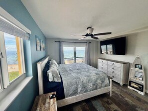 Ein Schlafzimmer mit einem Bett, einem Deckenventilator, einem Fernseher, einem Schminktisch und Blick aufs Meer.