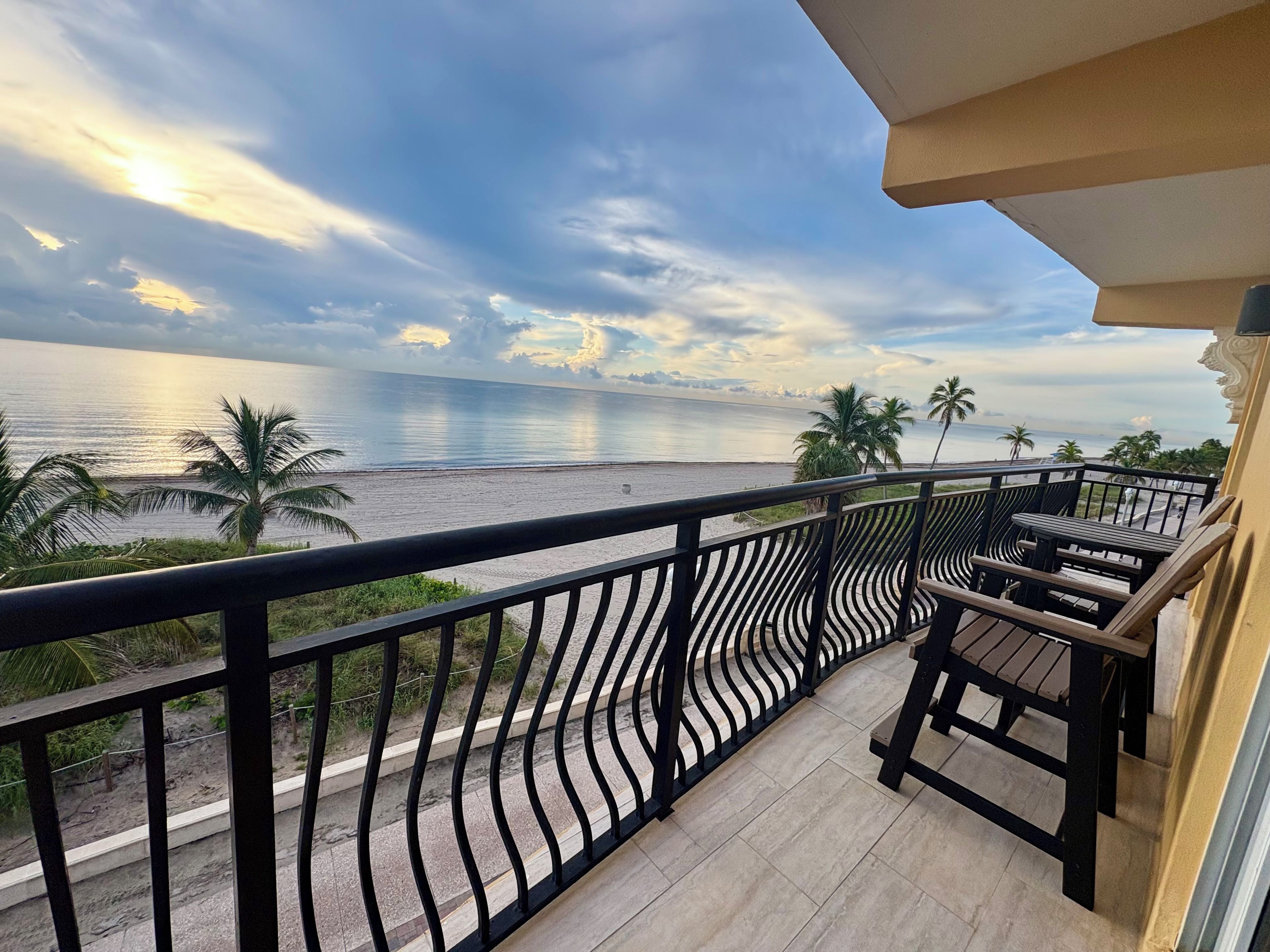 A balcony with a view of the sea and palm trees.
