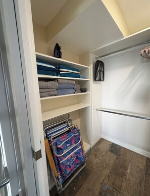 A walk-in closet with shelves for folded clothes, a hanging rack, and a storage unit with a colorful bag. - Beautiful Oceanview with Private Balcony on Hollywood Boardwalk (Hollywood)