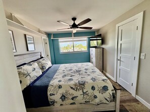 Een slaapkamer met een bed, een plafondventilator, een raam met uitzicht, een dressoir en een deur.