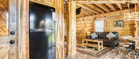 Interior de una cabaña de madera con un refrigerador negro, un sofá y una mesa de comedor.