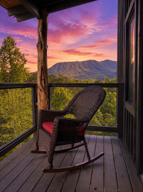 A rocking chair on a wooden deck with a view of a mountain range and trees. - 2-Bedroom Castle Cabin with Dungeon Game Room, Hot Tub & Mountain Views (Sevierville)