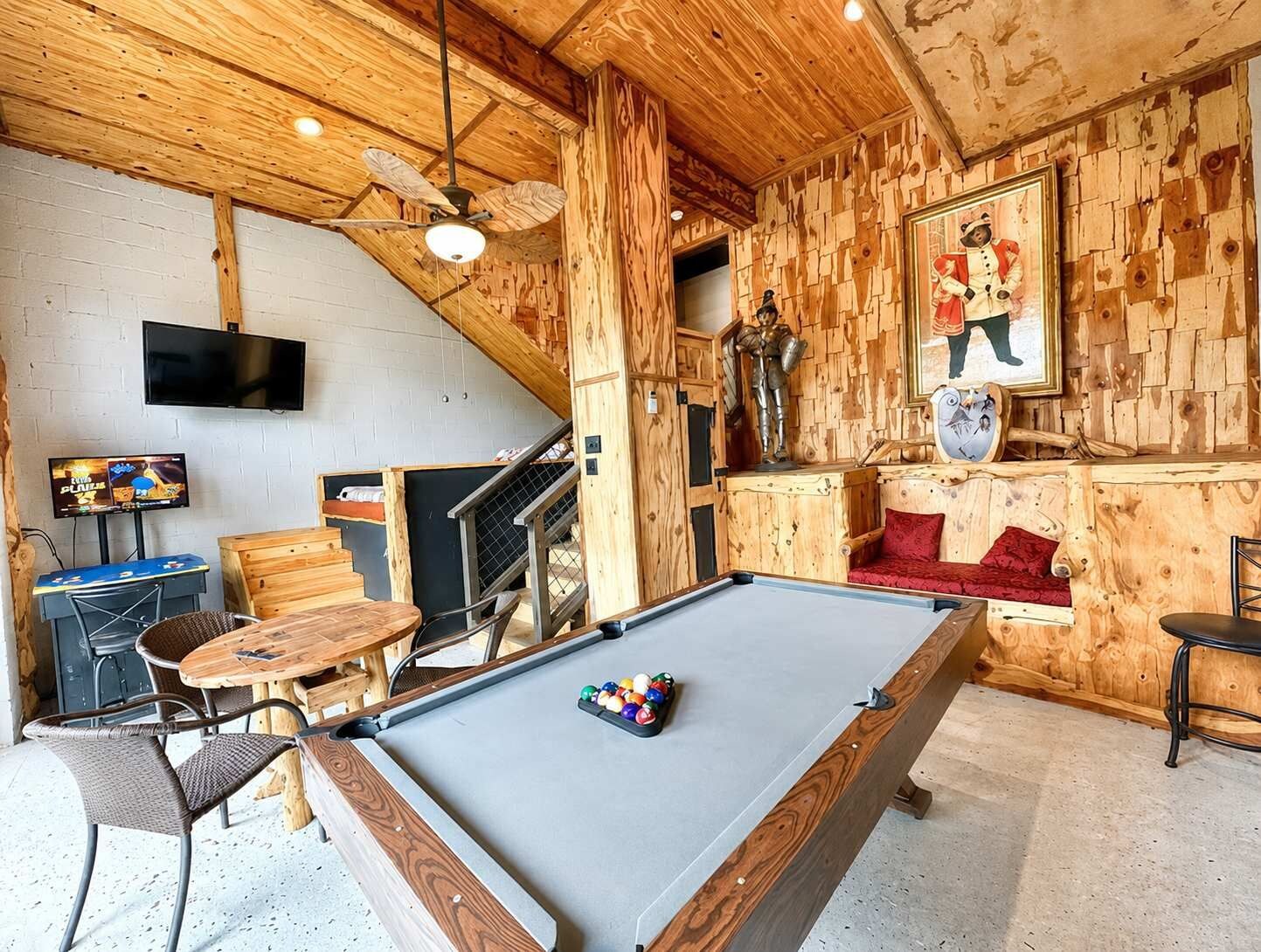 Una mesa de billar con bolas, un televisor y una pared de madera con una escalera.