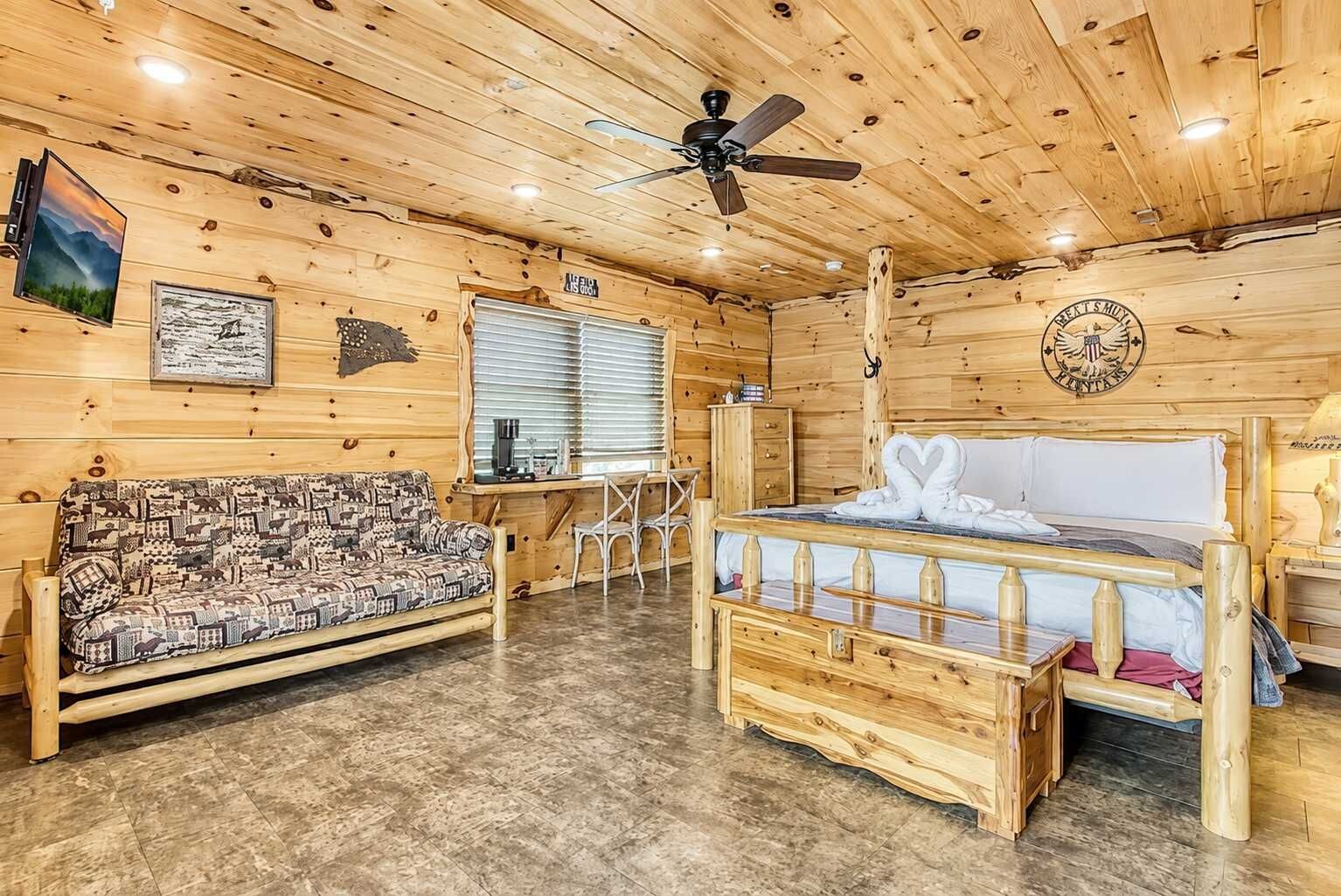 A wooden cabin interior with a bed, sofa, and a desk area.