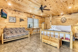 A wooden cabin interior with a bed, sofa, and a desk area. - 2-Bedroom Castle Cabin with Dungeon Game Room, Hot Tub & Mountain Views (Sevierville)