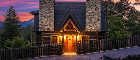 A log cabin with a stone chimney, wooden exterior, and a welcoming entrance.