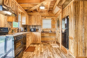 A rustic kitchen with wooden cabinetry, a stainless steel stove, and a refrigerator. - 2-Bedroom Castle Cabin with Dungeon Game Room, Hot Tub & Mountain Views (Sevierville)