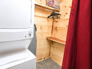 A compact room with a washing machine, wooden shelves, and a red curtain. - 2-Bedroom Castle Cabin with Dungeon Game Room, Hot Tub & Mountain Views (Sevierville)
