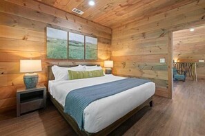 A wooden-paneled bedroom with a bed, bedside lamps, and a painting on the wall. - 4-Bedroom Cabin with Indoor Pool Waterfall & Game Room Near Pigeon Forge (Sevierville)