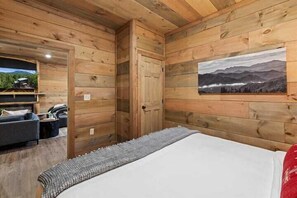 A wooden cabin room with a bed, a sofa, and a painting on the wall. - 4-Bedroom Cabin with Indoor Pool Waterfall & Game Room Near Pigeon Forge (Sevierville)