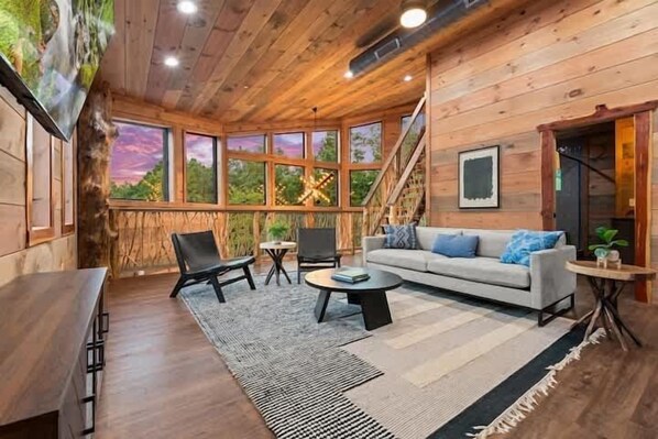 A wooden interior with a sofa, chairs, a coffee table, and a staircase. - 4-Bedroom Cabin with Indoor Pool Waterfall & Game Room Near Pigeon Forge (Sevierville)