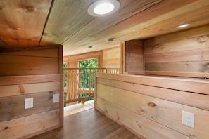 A wooden interior with a wooden floor, a ceiling with a light fixture, and a view of greenery outside. - 4-Bedroom Cabin with Indoor Pool Waterfall & Game Room Near Pigeon Forge (Sevierville)
