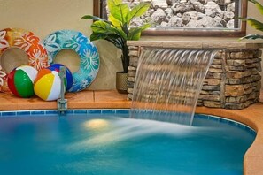 A swimming pool with a waterfall feature, surrounded by colorful inflatable rings and a potted plant. - 4-Bedroom Cabin with Indoor Pool Waterfall & Game Room Near Pigeon Forge (Sevierville)
