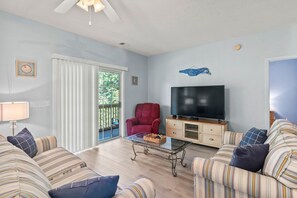 A living room with a television, sofa, armchair, and a glass coffee table. - Whale of a Tale | Beach Getaway + Pool + Screen (North Myrtle Beach)