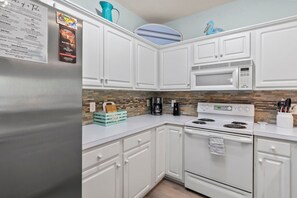 A kitchen with white cabinets, a stainless steel refrigerator, a microwave, and a stove. - Whale of a Tale | Beach Getaway + Pool + Screen (North Myrtle Beach)