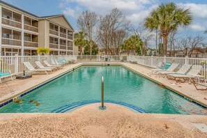 A swimming pool with lounge chairs, a white fence, and a building with balconies in the background. - Whale of a Tale | Beach Getaway + Pool + Screen (North Myrtle Beach)