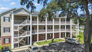 A multi-story residential building with a central courtyard, balconies, and a parking area. - Whale of a Tale | Beach Getaway + Pool + Screen (North Myrtle Beach)