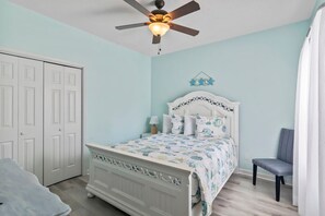 A bedroom with a bed, a chair, a ceiling fan, and a door. - Whale of a Tale | Beach Getaway + Pool + Screen (North Myrtle Beach)