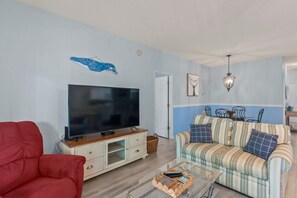 A living room with a television, red armchair, striped sofa, and a glass coffee table. - Whale of a Tale | Beach Getaway + Pool + Screen (North Myrtle Beach)