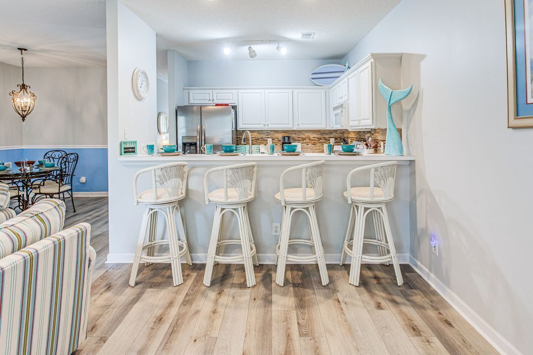 Une cuisine avec des meubles blancs, un îlot central doté de tabourets de bar et un élément décoratif bleu sur le mur.