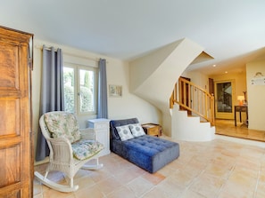 A room with a wooden rocking chair, a small white chest of drawers, a blue sofa, and a staircase leading to another area. - Le Petit Mas - Piscine - Golf de Pont Royal (Mallemort)
