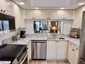 A modern kitchen with white cabinetry, a stainless steel dishwasher, a built-in oven, and a large flat-screen TV. - 4108 - Beautifully Updated 2-bed/2-bath condo close to Beaches and IMG Academies (Bradenton)