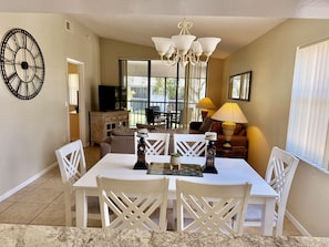A dining area with a white table and chairs, a chandelier, and a large wall clock.