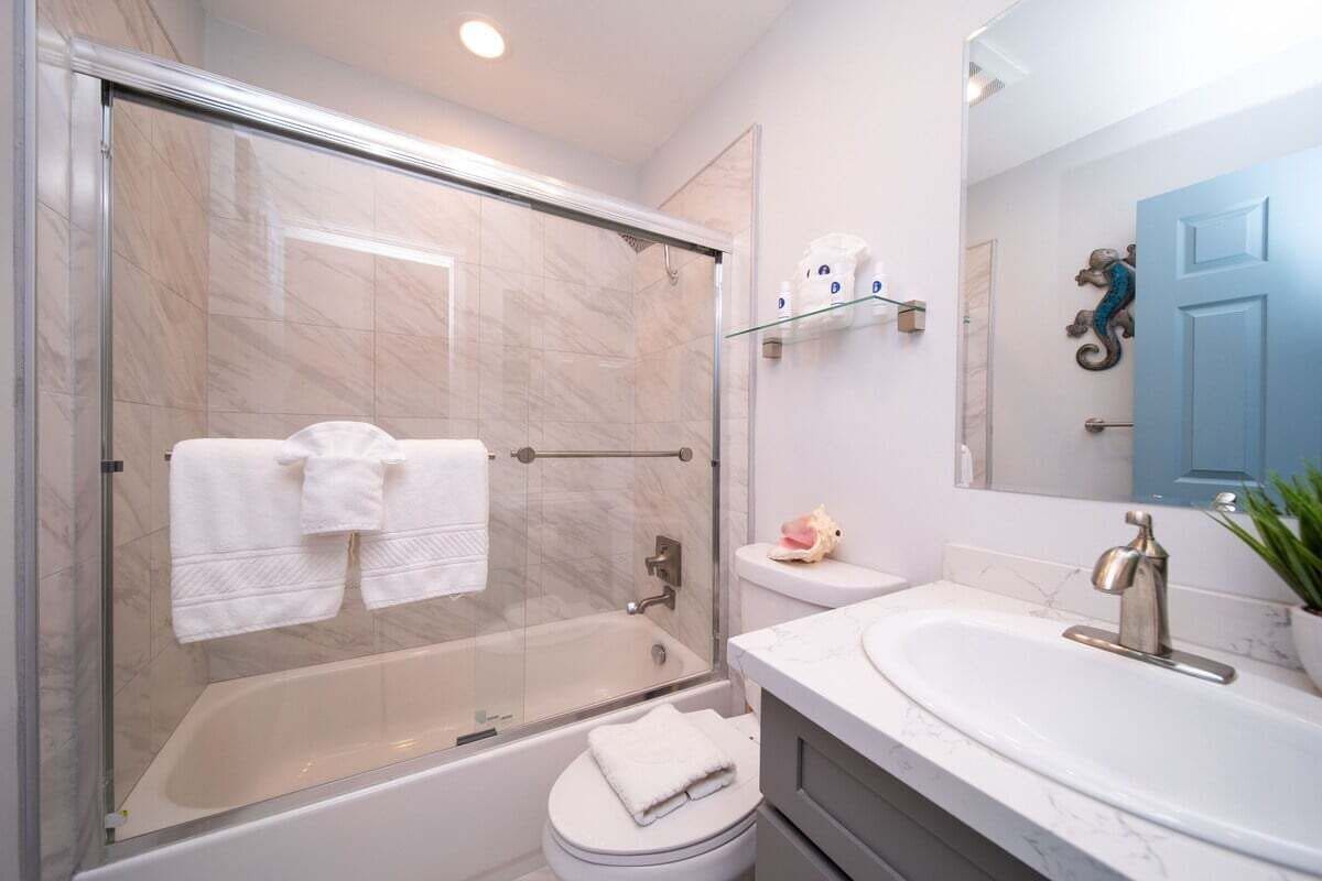 Ein Badezimmer mit einer Duschkabine, einer weißen Toilette, einem Waschbecken mit Marmorplatte und einem Spiegel über dem Waschbecken.