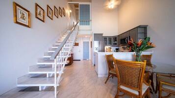 A modern kitchen with white cabinets, a dining area with wicker chairs, and a staircase leading to an upper level.