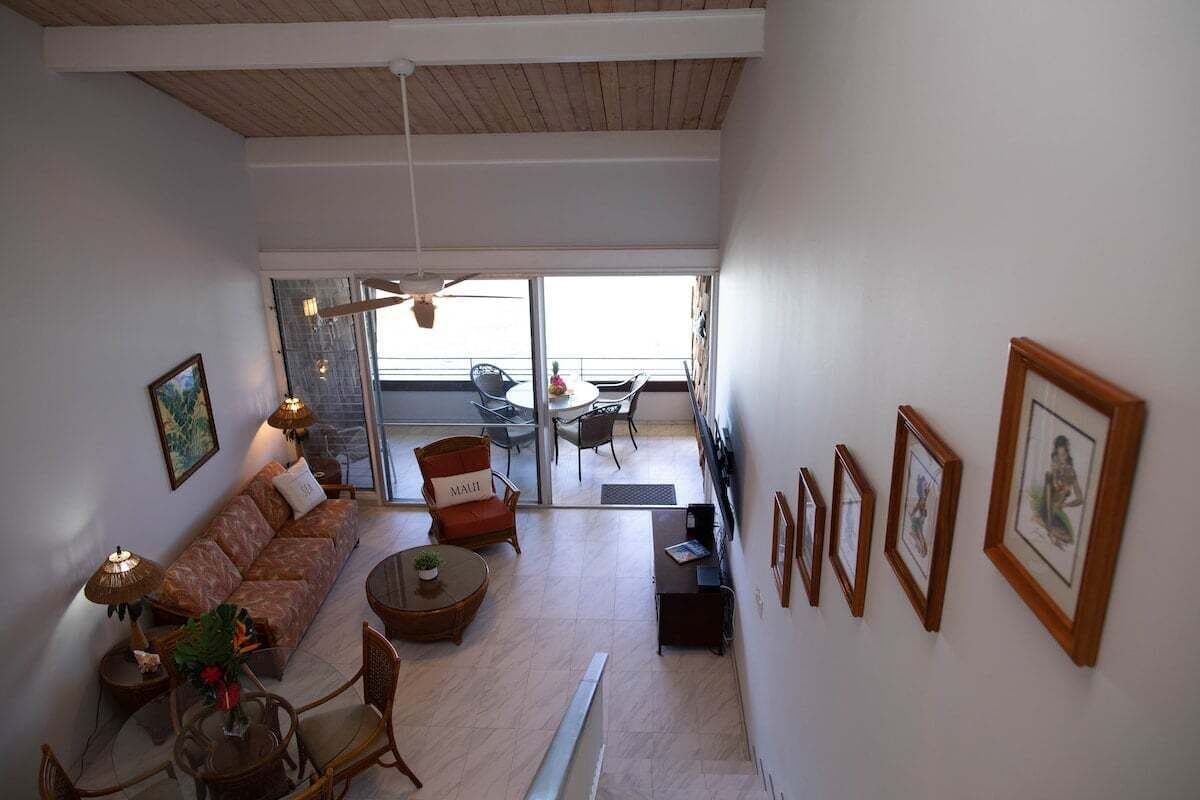 A spacious living area with a sofa, chairs, a dining table, and a balcony with outdoor seating.