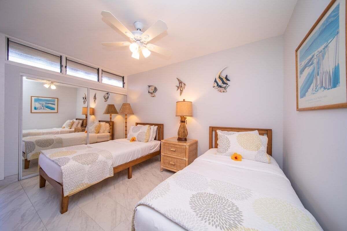 Une chambre d’hôtel avec deux lits, un ventilateur de plafond, des œuvres d ’art murales et une grande fenêtre.