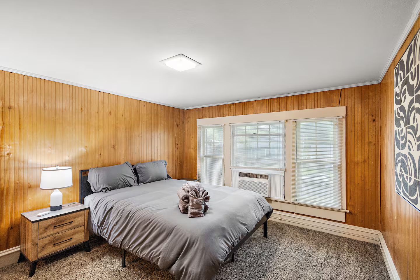 Un dormitorio con cama, mesita de noche, lámpara y una ventana con persianas.