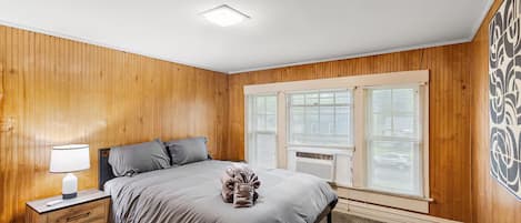 Un dormitorio con cama, mesita de noche, lámpara y una ventana con persianas.